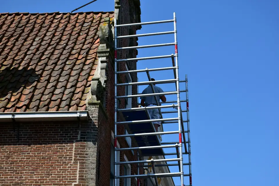 Échafaudage dressé contre une façade en brique sous un toit de tuiles