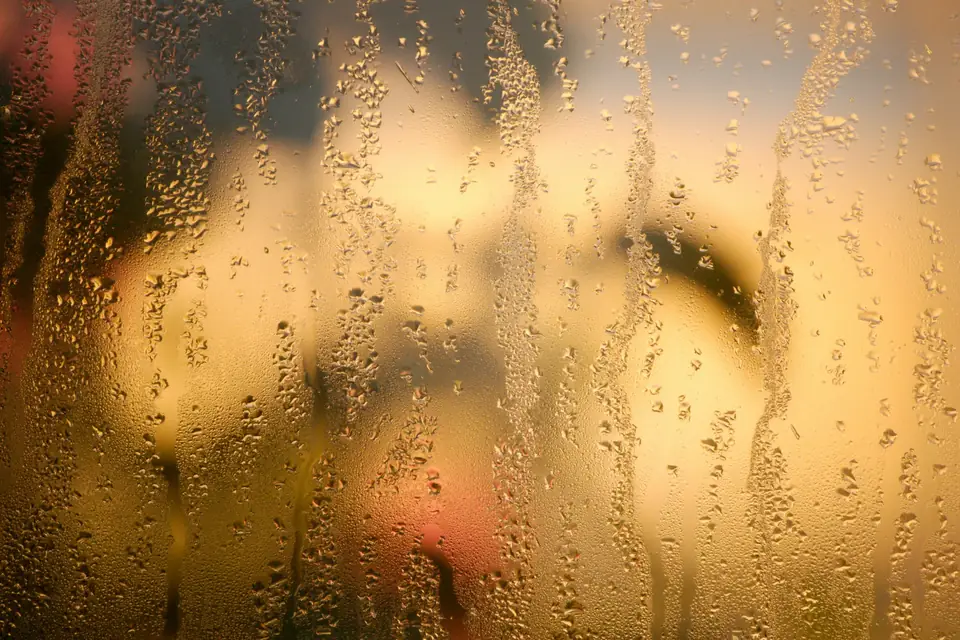 Gouttes d’eau sur une vitre, lumière chaude derrière