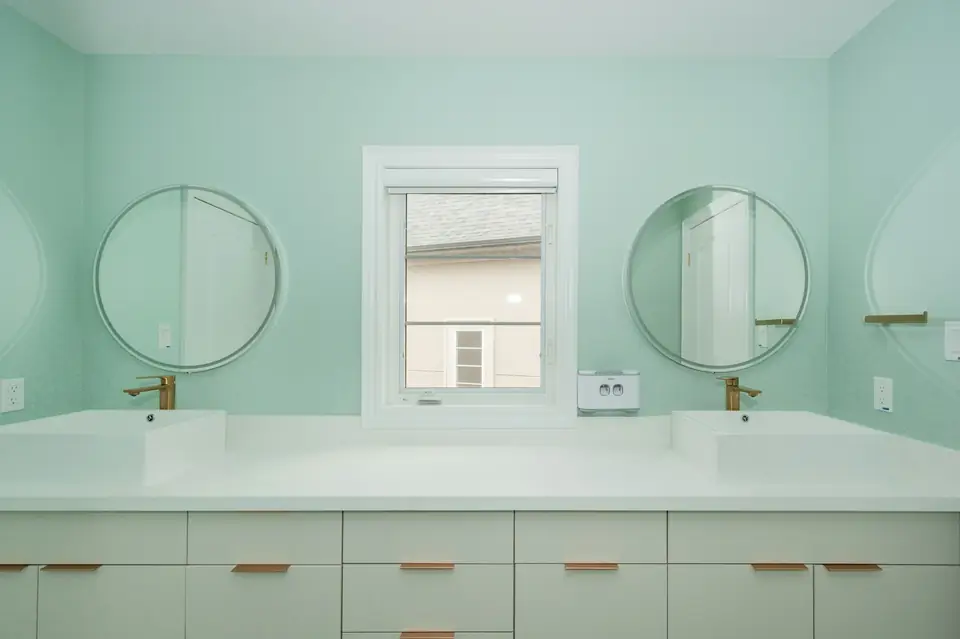 Salle de bain aux murs vert menthe, double vasque et deux miroirs ronds